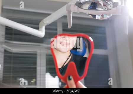 Frau prüft Zähne im Spiegel. Lächelnde Frau im Zahnarztpraxis. Lächeln Sie breiter und schön sein. Stockfoto