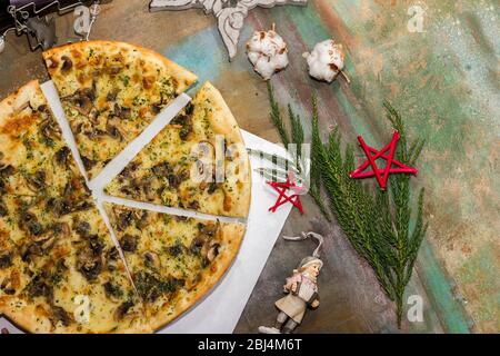 Pizza mit Pilzen und Käse auf einem festlichen Tisch, bestreut mit trockenen italienischen Kräutern. Vor dem Hintergrund der Neujahrsspielzeuge Stockfoto