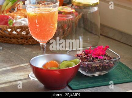 Vitamine für einen gesunden Lebensstil: Scheiben Kiwi und Clementine in einer roten Schüssel, getrocknete Teeblätter in einer Schüssel, frischer Orangensaft Stockfoto