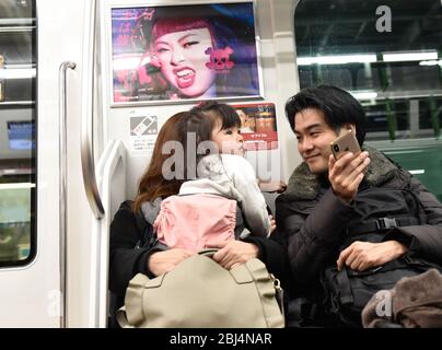 Eltern mit ihrem kleinen Kleinkind fahren mit dem Zug nach Hause und unterhalten das Kind mit ihrem Smartphone in Tokio, Japan. Stockfoto