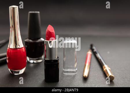 Kosmetikprodukte in Rot und Schwarz herstellen. Roter Lippenstift und nagellack, Augenstift und Bürsten vor schwarzem Farbhintergrund Stockfoto