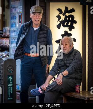 Zwei ältere japanische Männer aus der Gegend beobachten die vorbeigehenden Leute und reden. Enoshima Haupteinkaufsstraße, Enoshima Insel, Japan Stockfoto