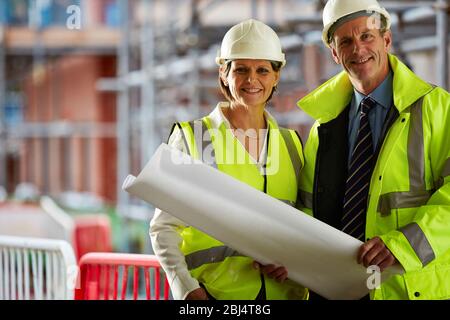 Porträt von zwei reifen Architekten in Schutzkleidung auf der Baustelle Blick auf Kamera hält eine Blaupause Stockfoto