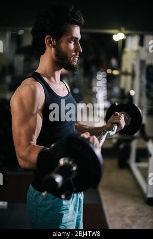Seitenansicht des sportlichen bärtigen jungen Mannes mit muskulösem Körper, der mit Langhantel arbeitet Stockfoto