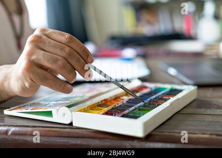 Mann Künstler Malerei mit Pinsel und Aquarell Palette auf Skizzenbuch. Nahaufnahme. Selektiver Fokus. Stockfoto