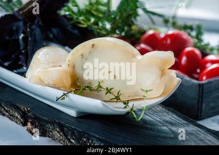 Frischer, traditioneller italienischer Kuh- oder Ziege- und Schafskäse, halbsüß Caciocavallo, Scamorza mit aromatischen Kräutern im Schnitt. Auf einem Teller mit Tomaten und Stockfoto