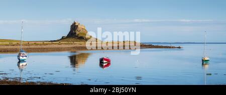 Ein Panoramabild der Burg auf der Heiligen Insel mit Booten im Vordergrund bei Flut. Stockfoto