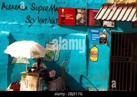 Ein Mann repariert Kleidung vor einem Township Supermarkt in Johannesburg in Südafrika. Stockfoto