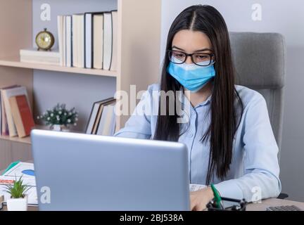 Geschäftsfrau mit Maske im Gesicht, die während der Coronavirus-Pandemie im Büro arbeitet. Arbeiten zu Hause während des Pandemiekonzepts. Stockfoto