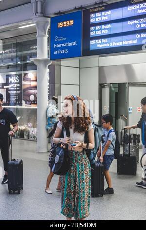 London/UK-26/07/18: Eine junge Frau mit rothaarigen Haaren steht in der Ankunftszone der Eurostar-Züge in St Pancras International, schaut zur Seite, Liste Stockfoto