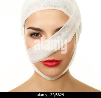 Junge verspielte Frau mit einem Gaze-Verband auf Kopf und Brust, auf schwarzem Hintergrund Stockfoto