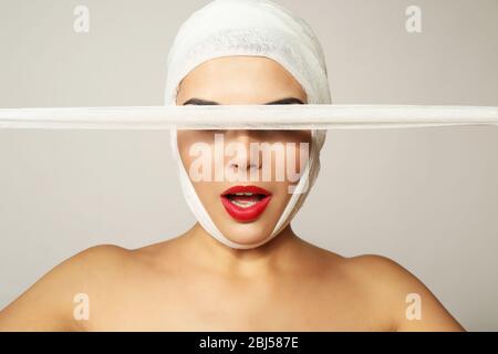 Junge schöne Frau schließt ihr Gesicht mit Gaze, auf grauem Hintergrund Stockfoto