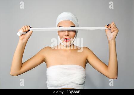 Junge schöne Frau schließt ihr Gesicht mit Gaze, auf grauem Hintergrund Stockfoto