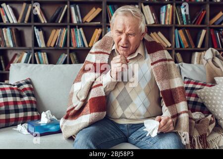 Der ältere Mann allein sitzt in der Bibliothek mit karierten, das Gewebe Husten bedeckt hält Stockfoto