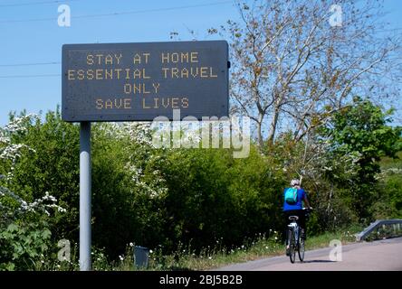 Reading, Großbritannien - April 26 2020: Ein Radfahrer fährt unter einem Schild, das die Menschen darauf hinführt, während der Sperrung des Corvid-19 auf Basingstoke R zu Hause zu bleiben Stockfoto