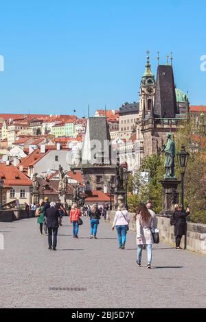 Prag, Tschechische Republik - 23. April 2020: Ehepaar mittleren Alters, die auf der Karlsbrücke mit medizinischen Gesichtsmasken spazieren. Statuen auf der Brücke. Stadtzentrum während der Coronavirus-Pandemie. COVID-19-Krise. Stockfoto