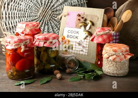 Gläser mit eingelegtem Gemüse und Bohnen, Gewürze, Buch der Rezepte und Küchenutensilien auf Holzhintergrund Stockfoto