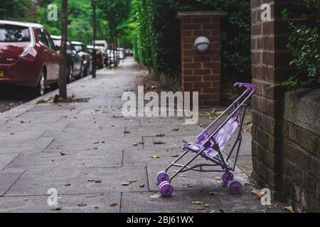 Der lila Kinderwagen ist auf einer Straße in einer Stadt links. Kinderwagen werden für die kleinen Kinder bis etwa drei Jahre verwendet, in denen die Kinder in einer sitzenden Position sind Stockfoto