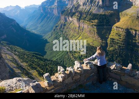 Eine Frau von hinten auf einem Balkon des Ordesa Nationalparks, die von der Spitze des Berges das ganze Tal, die grünen Wälder, die Felsen, die hil bewundert Stockfoto