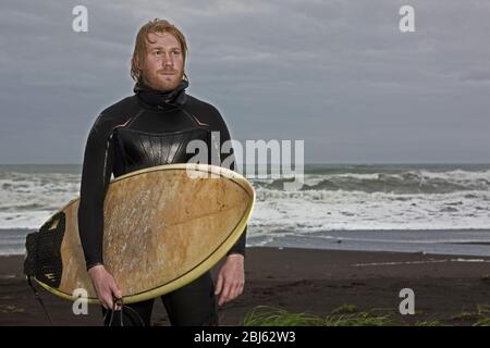 Junger Mann spaziert mit Surfbrett am Strand in Island entlang Stockfoto