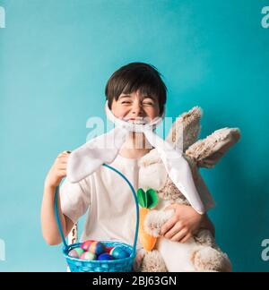 Junge mit Hasenohren, der Spielzeugkaninchen und ostereier in einem Korb hält. Stockfoto