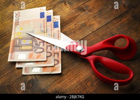 Schere schneidet Euro-Banknote auf Holzhintergrund Stockfoto