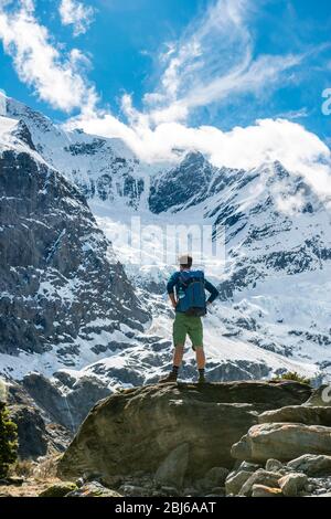 Bergsteiger steht auf Felsen, beeindruckende Aussicht auf Rob Roy Gletscher, Mount Aspiring National Park, Otago, South Island, Neuseeland Stockfoto