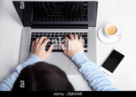 Frau, die mit einem Laptop arbeitet, auf einem Holzschreibtisch. Draufsicht Stockfoto
