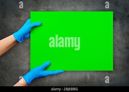 Leere grüne Karte in Arzthand in blauen Handschuhen mit Kopierraum, auf grauer Zementmörtel-Wand. Stockfoto