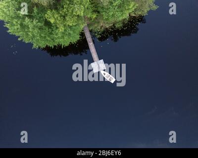 Luftaufnahme zum Pier mit einem Boot mit reflektierenden Wolken im Wasser, auf einer kleinen grünen Insel Stockfoto