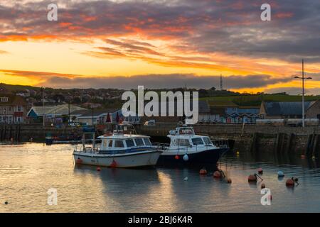 West Bay, Dorset, Großbritannien. April 2020. Wetter in Großbritannien. Der Himmel leuchtet orange, während die Wolken über dem Hafen bei Sonnenuntergang im Seebad West Bay in Dorset nach einem Tag mit leichtem Regen und bewölktem Himmel klar werden. Bild: Graham Hunt/Alamy Live News Stockfoto