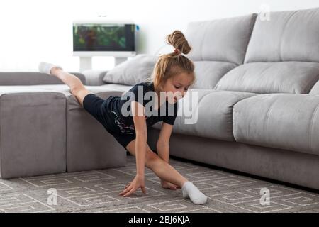 Vollgarn durchführen. Elastische kleine Mädchen tun Gymnastik auf Möbeln im Wohnzimmer in hellem Tageslicht Stockfoto