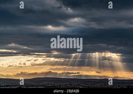 Panoramablick auf den dramatischen Sonnenstrahl durch niedrige Wolken über der Stadt bei Sonnenuntergang. Die Sonne schneidet durch die Wolken über der Stadt. Sonnenstrahlen auf die Stadt Stockfoto