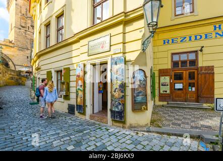 Ein junges Paar schaut in das Fenster eines Marionetten- und Puppenladens auf der Prager Kampa-Insel, hinter dem sich einer der gotischen Türme befindet. Stockfoto