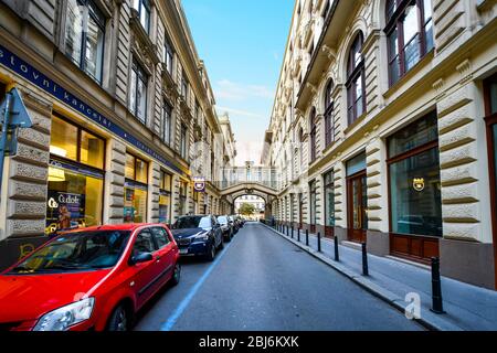 Autos parken entlang einer Einbahnstraße mit einer Fußgängerbrücke in Sicht im modernen Finanzviertel von Budapest, Ungarn. Stockfoto