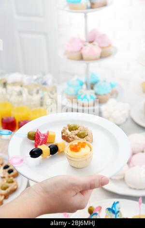 Frau hält Teller mit Snacks und Kanape auf Buffet Hintergrund Stockfoto
