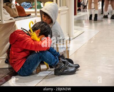 Zwei japanische Brüder sitzen auf dem Boden und warten auf ihre Mutter, während sie in einem Geschäft im Shibuya 109 Kaufhaus nach Kleidung kauft. Stockfoto