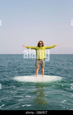 Glücklicher, lächelnder männlicher Tourist auf einem Bootsausflug und genießen das Reiserlebnis, auf einem Salzschornstein im Toten Meer, Israel, zu stehen Stockfoto