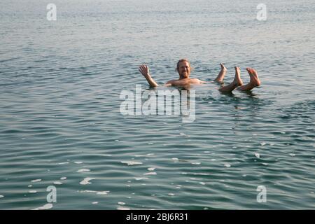 Fröhlicher lächelnder Mann, der auf seinem Rücken im Toten Meer schwimmt Stockfoto