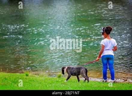 Ein Mädchen geht mit ihrem brindle Pitbull Terrier Welpen am See im Langan Park, 13. April 2019, in Mobile, Alabama. Stockfoto