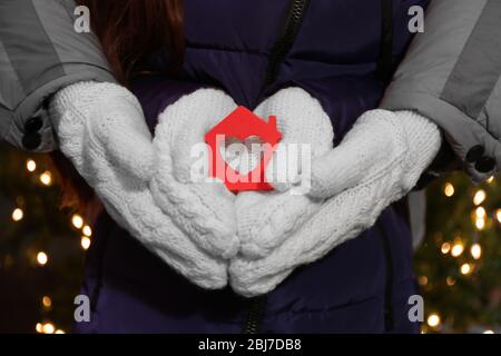 Hände halten winziges Haus mit Herz auf beleuchteten Hintergrund Stockfoto