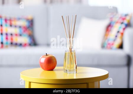 Handgefertigter Reed-Freshener mit rotem Apfel auf gelbem Tisch im Wohnzimmer, aus nächster Nähe Stockfoto