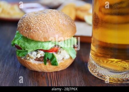 Großer leckerer Hamburger mit Glas Becher helles Bier auf dunklem Holzhintergrund, Nahaufnahme Stockfoto