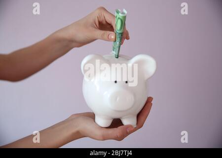 Weibliche Hände halten und setzen Euro-Banknote in weißen Sparschwein, Nahaufnahme Stockfoto