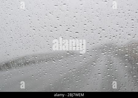 Regentropfen auf einem grauen Autofenster auf einem Autobahnhintergrund Stockfoto