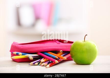 Apfel und Bleistiftbox voll mit Bleistiften auf dem Tisch im Zimmer Stockfoto