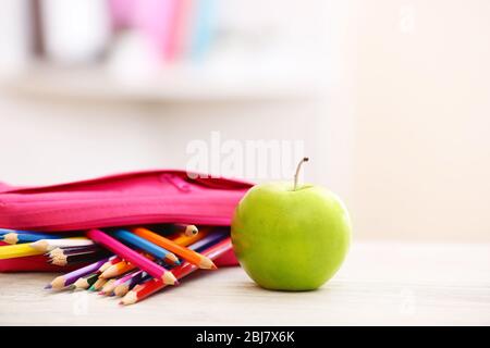 Apfel und Bleistiftbox voll mit Bleistiften auf dem Tisch im Zimmer Stockfoto
