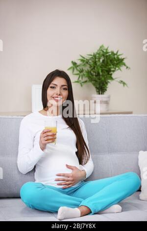 Schwangere Frau auf dem Sofa und trinken Orangensaft im Zimmer Stockfoto