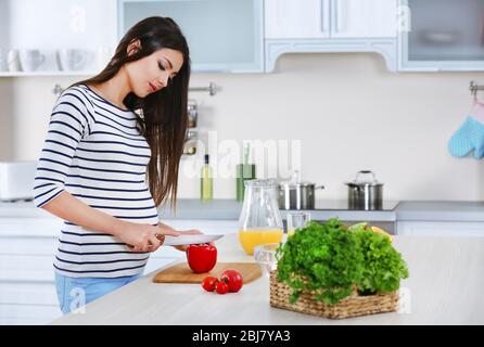 Schwangere Frau bereitet Gemüsesalat am Tisch in der Küche Stockfoto