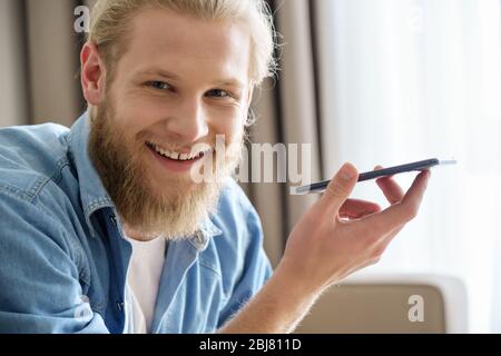 Glücklich junge Mann, der Telefon mit virtuellen Sprachassistenten Blick auf Kamera. Stockfoto
